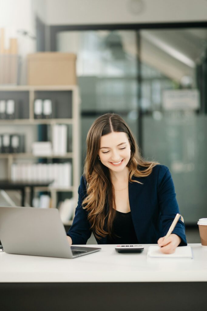 Jonge vrouw die in haar home office aan tafel aan het werken is aan de computer
